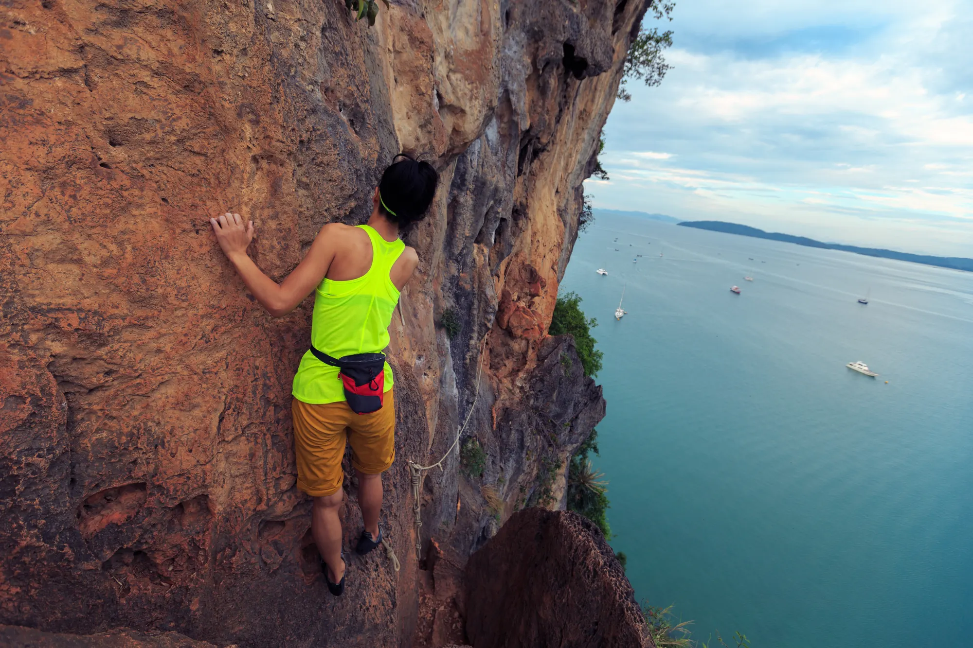 Escaladora subindo uma parede de rocha acima do mar