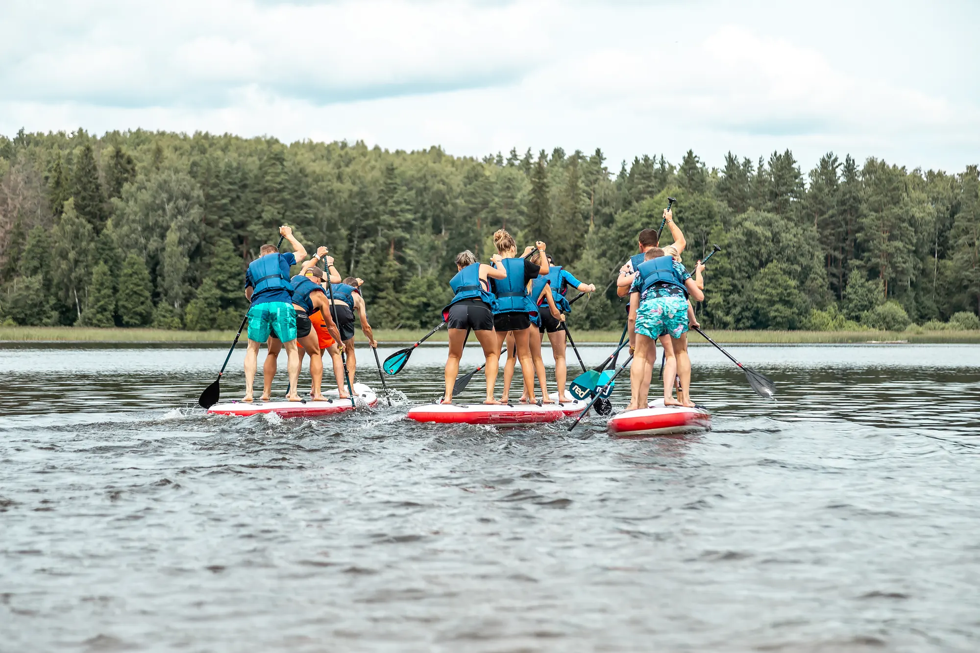 Grupo remando stand up paddle em uma lagoa cercada de mata
